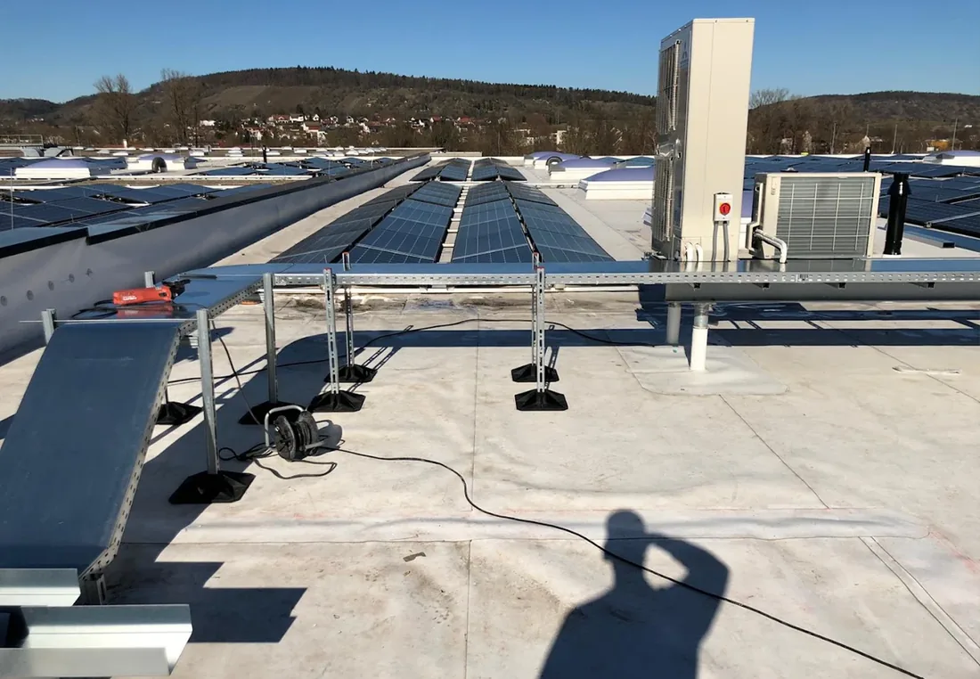 Klima-Außengerät auf einer Ständerkonstruktion neben Photovoltaikmodulen auf einem Industriedach